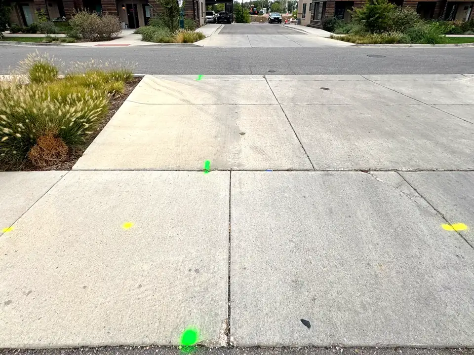 Green and yellow locate marks on a concrete sidewalk at a street crossing